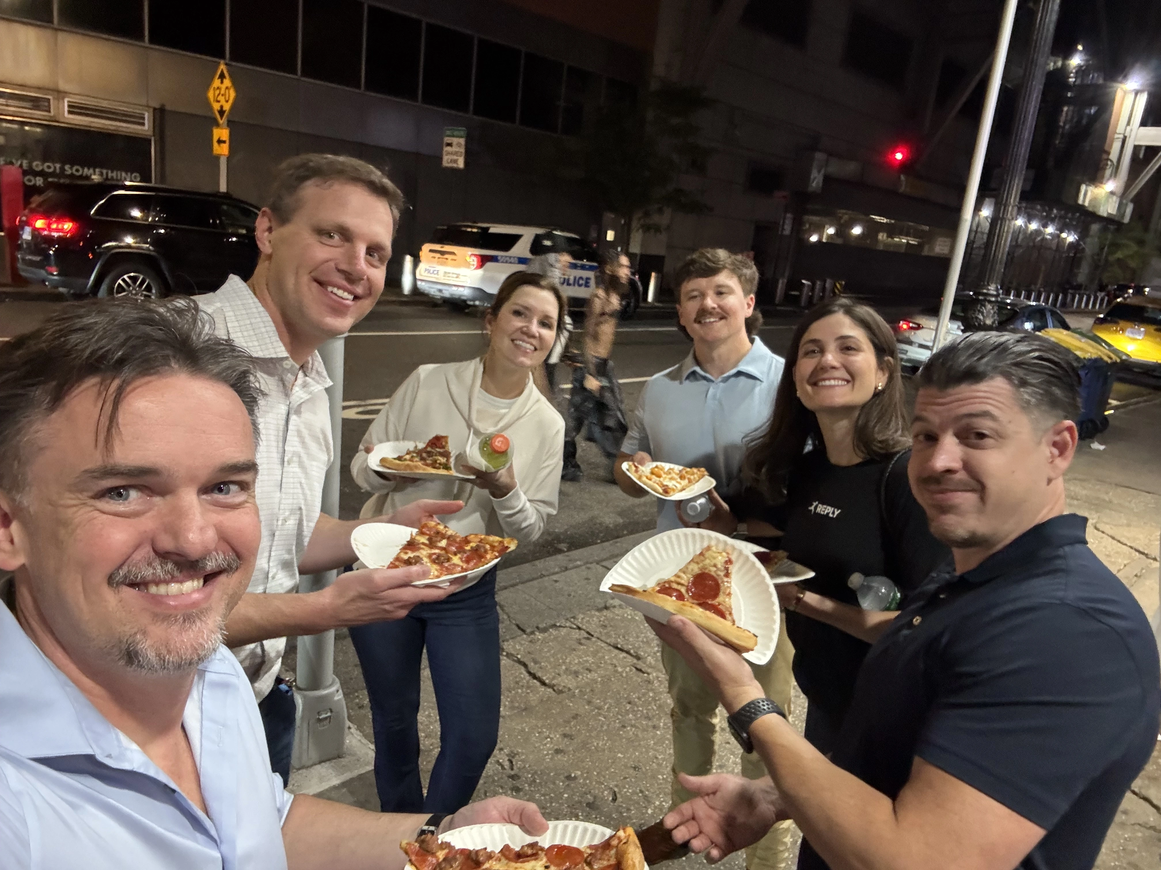 Six Sagepath Reply reps enjoying street pizza and laughs under city lights after an Opticon 2025 event.
