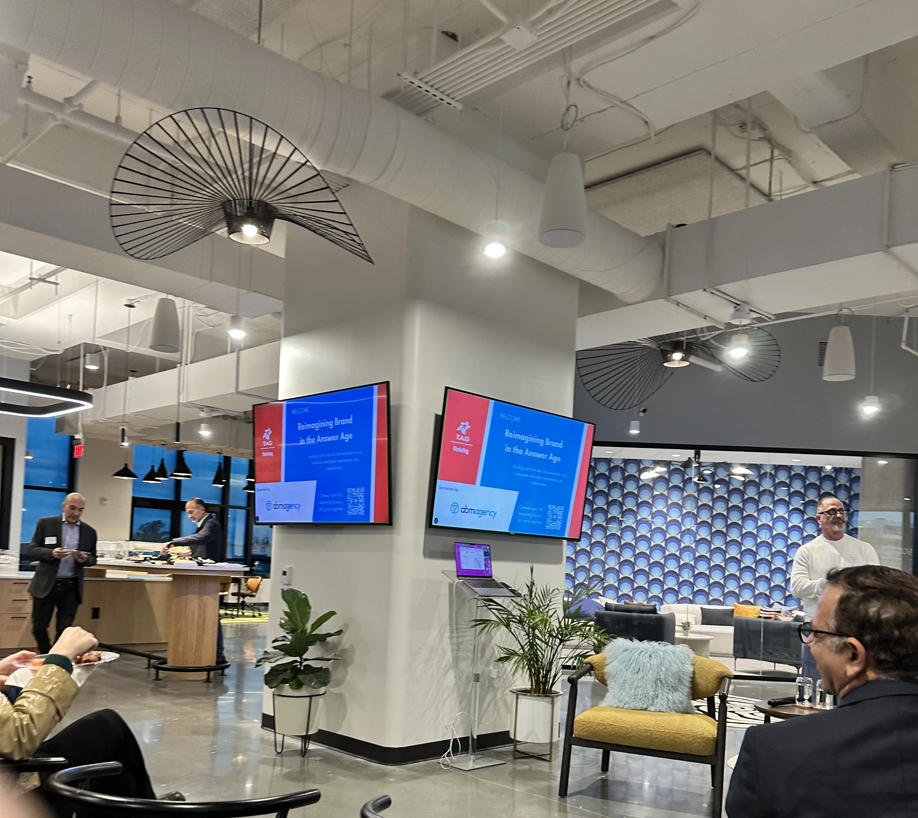 A speaker presents on answer engine optimization with supporting slides in a modern office with seated attendees.