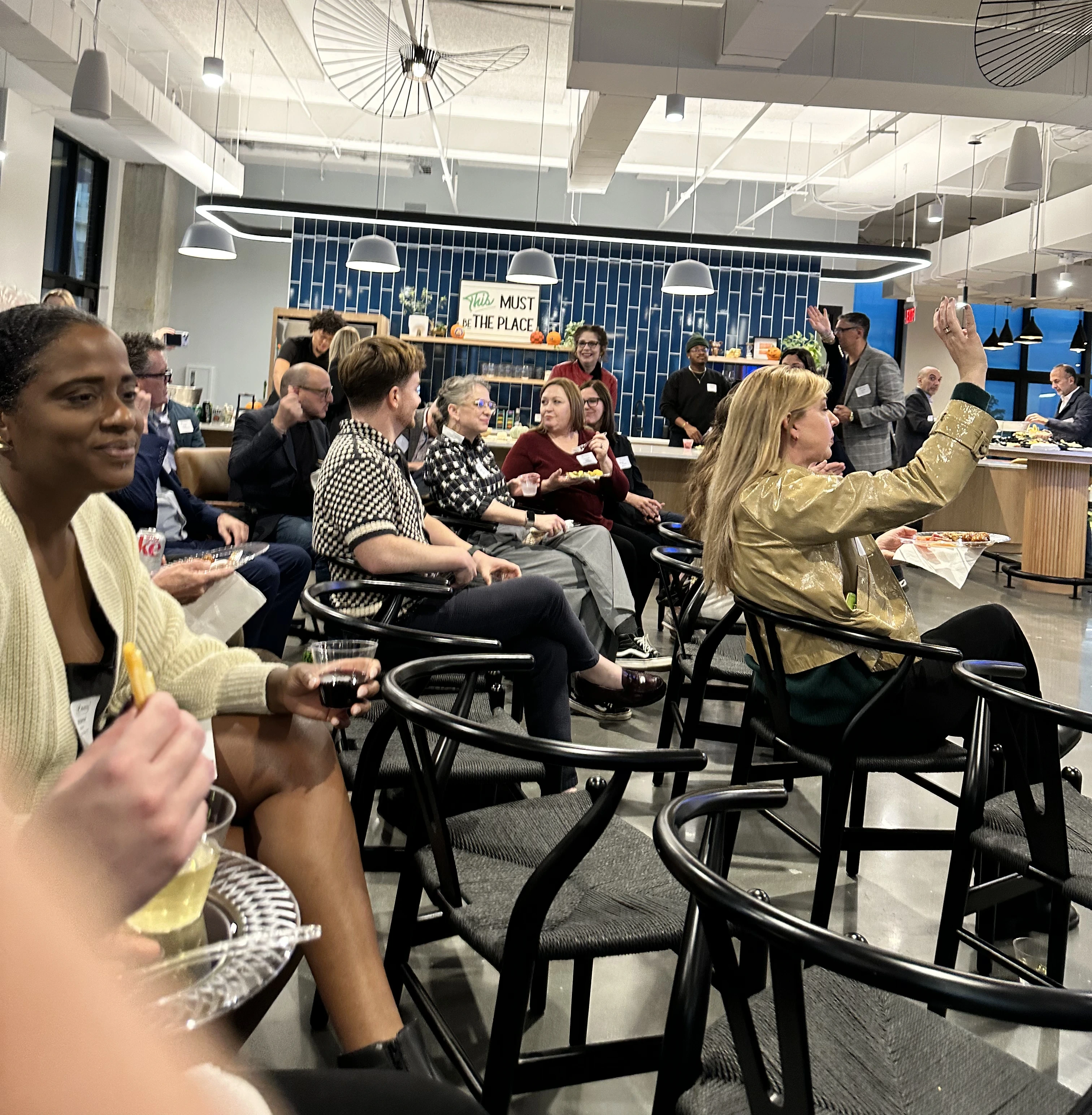 Attendees at a talk on answer engine optimization sit in a modern office space, some eating, one raising a hand to speak.