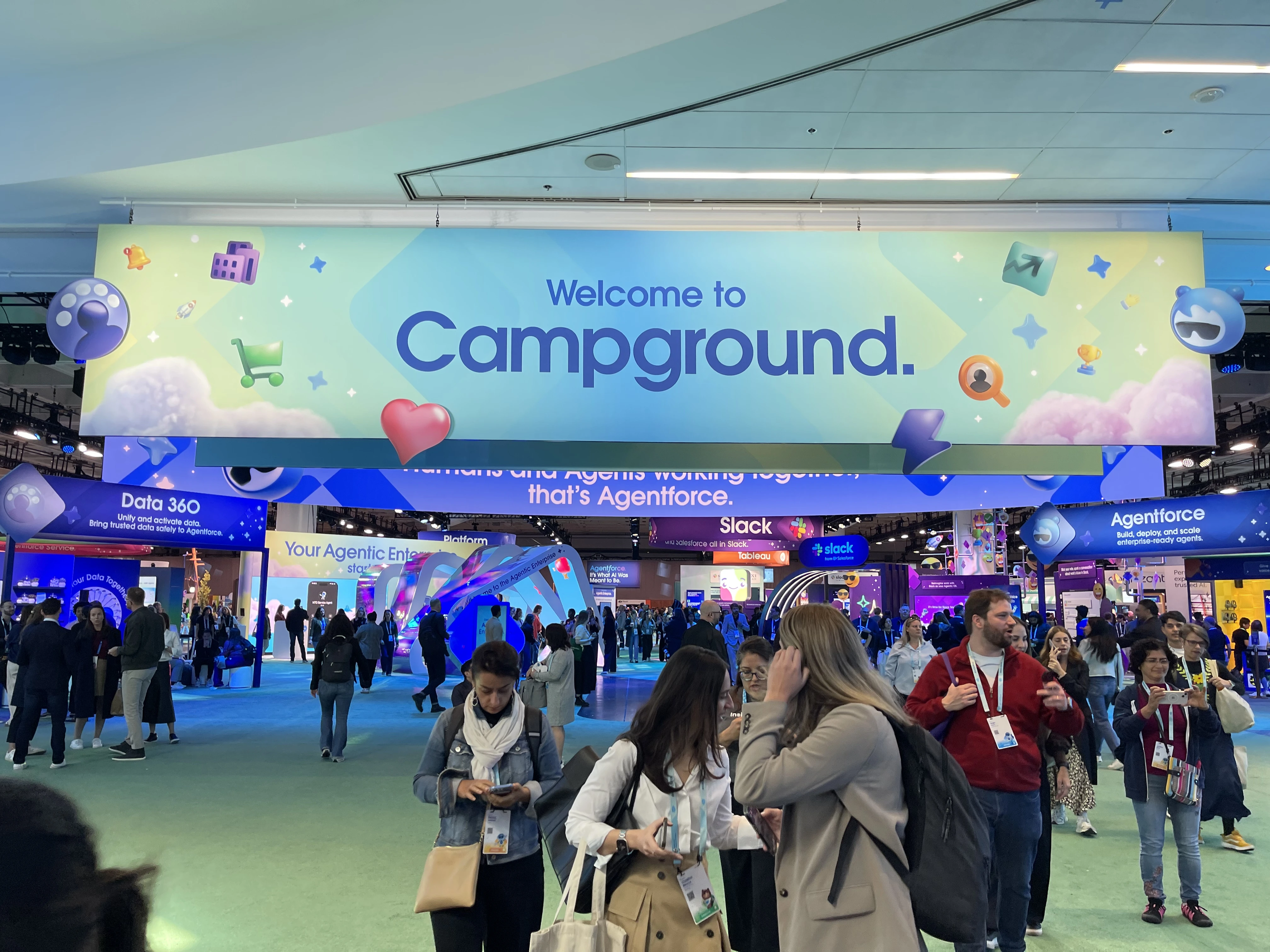 Attendees navigate the bustling indoor Campground zone at Salesforce Dreamforce 2025, surrounded by signage for Slack, Agentforce, and other customer engagement platforms.