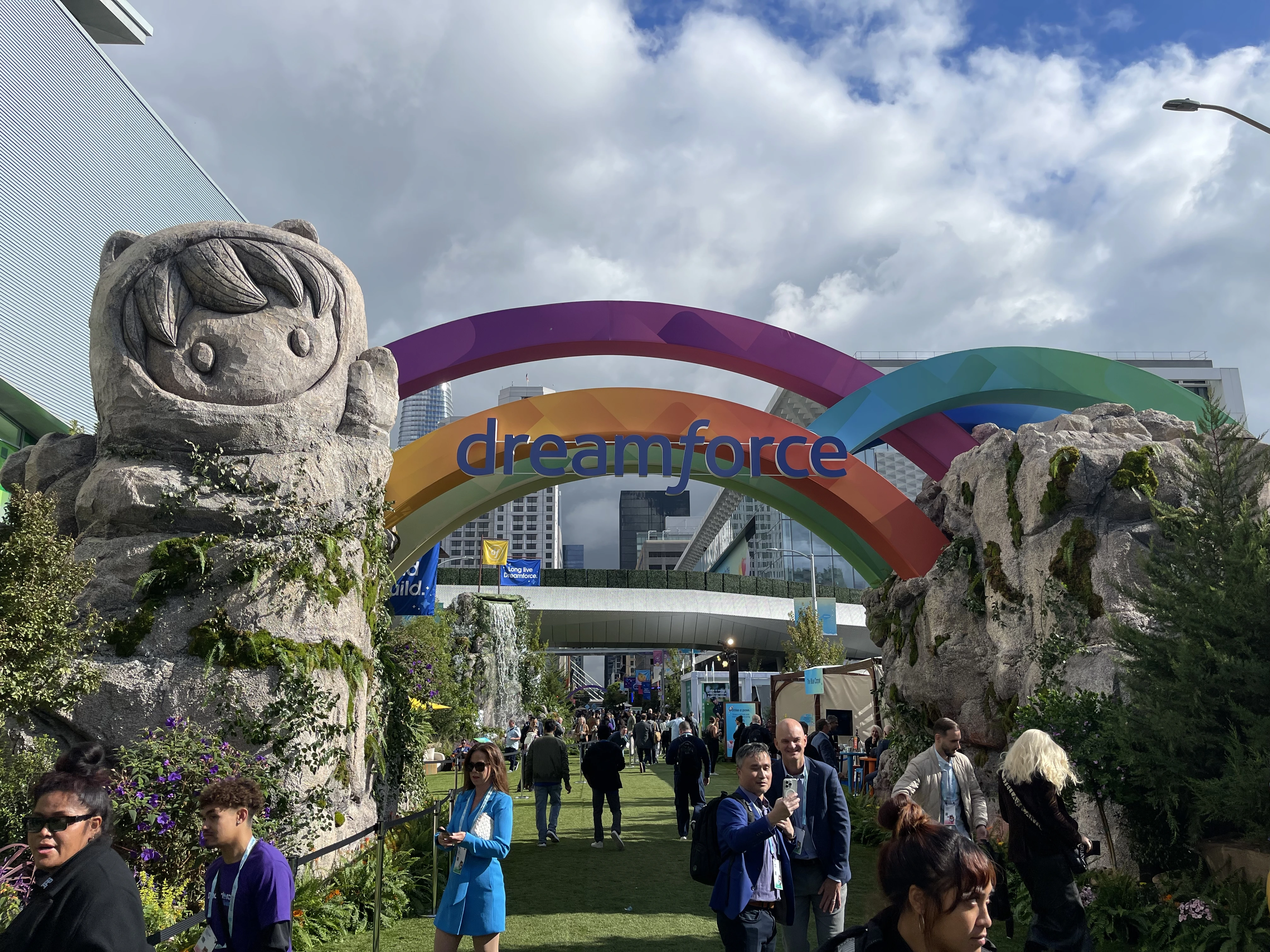 The entrance to Dreamforce 2025 features a rainbow-colored arch with the Salesforce logo and cartoonish stone mascots, welcoming attendees to the customer experience event.