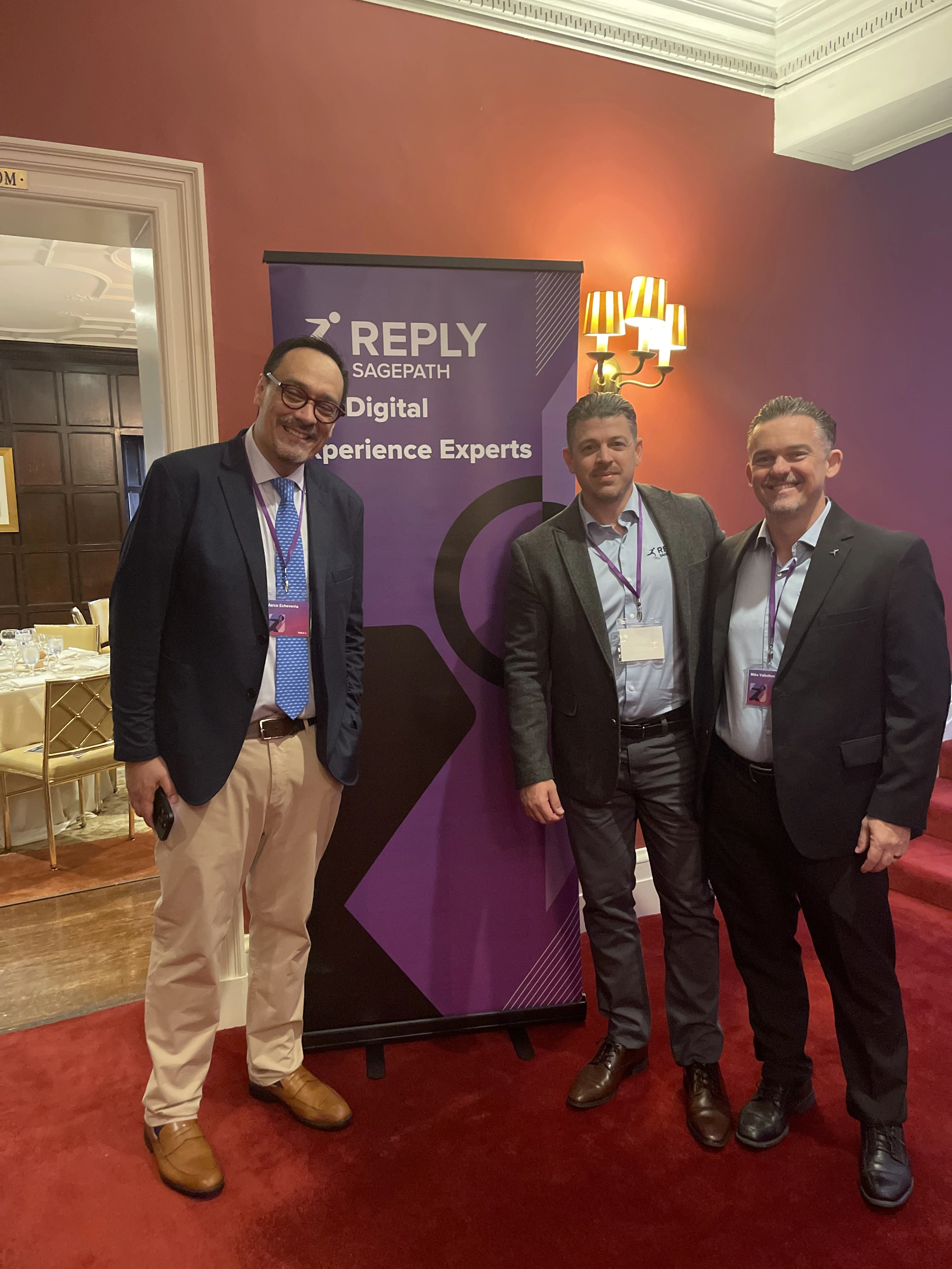 Smiling Sagepath Reply team members next to a branded banner at Harvard Club during Opticon 2025.